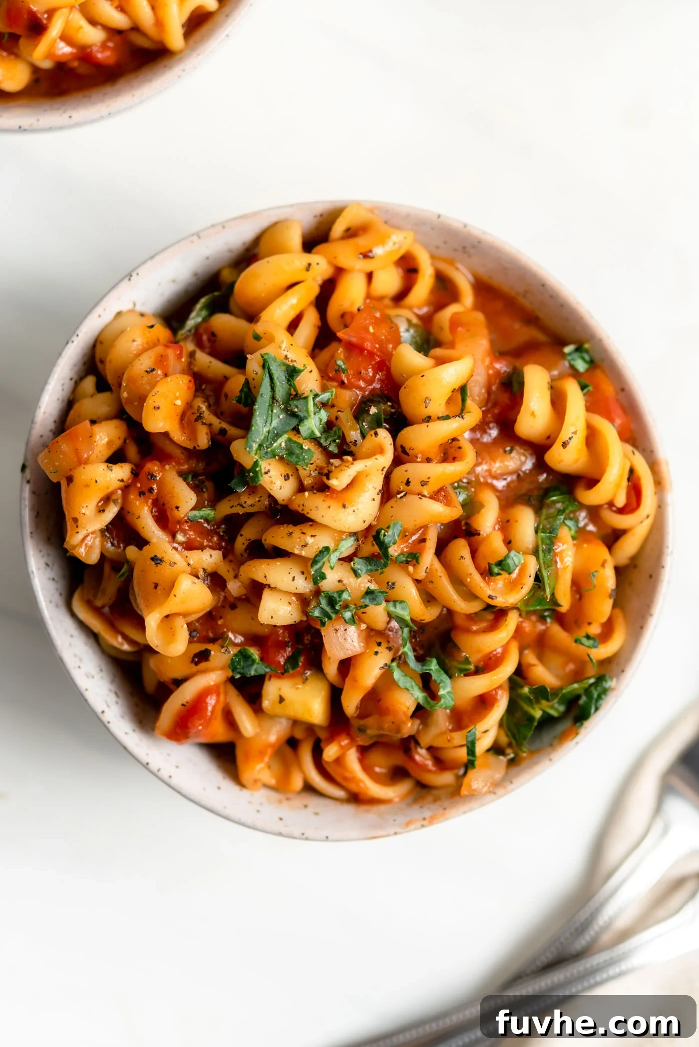A vibrant bowl of vegan one-pot pasta featuring rotini in a rich tomato sauce, generously mixed with sautéed mushrooms, onions, bell peppers, and zucchini. Fresh herbs garnish the top.