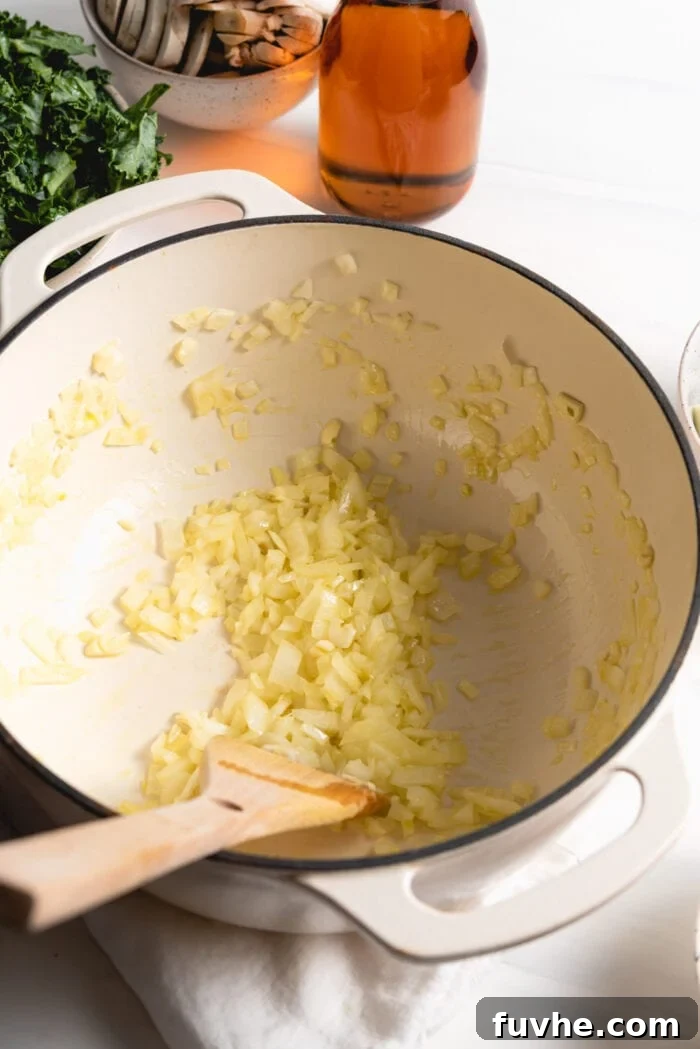 Chopped white onions and minced garlic gently cooking in olive oil in a large, heavy-bottomed pot over medium heat, stirred with a wooden spoon.