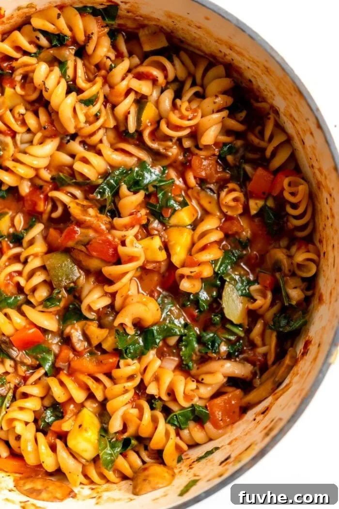 A large pot filled with perfectly cooked rotini pasta, vibrant green kale, and tender vegetables, all bathed in a rich tomato sauce, ready to be served.