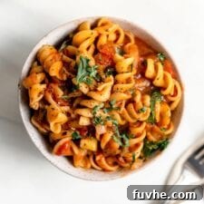 Overhead view of a bowl of rotini pasta with tomato sauce and vegetables.