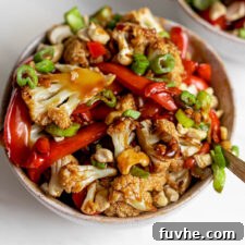 Bowl of cauliflower kung pao topped with chopped green onions and cashews.