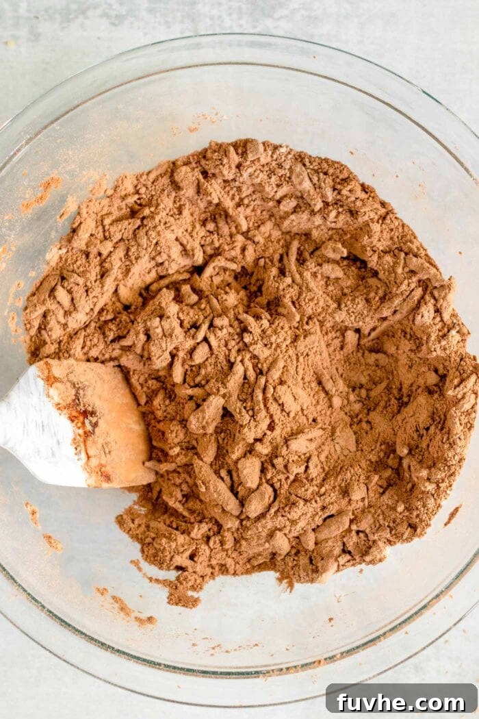 Fudgy Plant-Based Chocolate Zucchini Loaf 5 Spatula mixing grated zucchini into flour and cocoa powder in a glass mixing bowl.