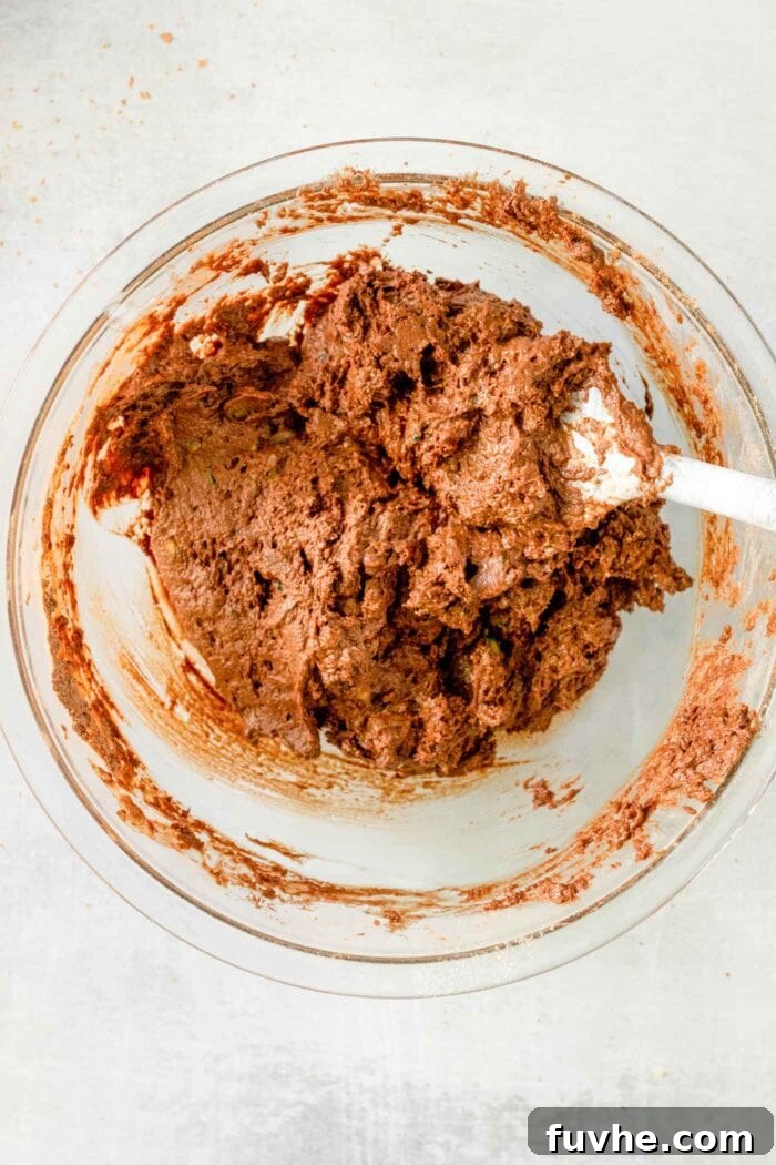 Fudgy Plant-Based Chocolate Zucchini Loaf 7 A thick chocolate batter being mixed with a wooden spoon in a mixing bowl.