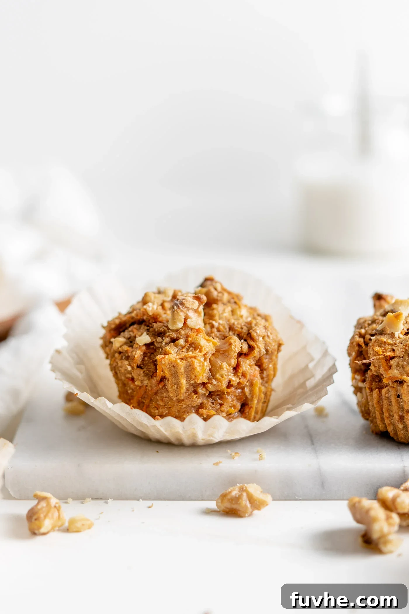 Small carrot muffin in a cupcake liner sitting on a marble cutting board, highlighting its moist texture and wholesome ingredients.