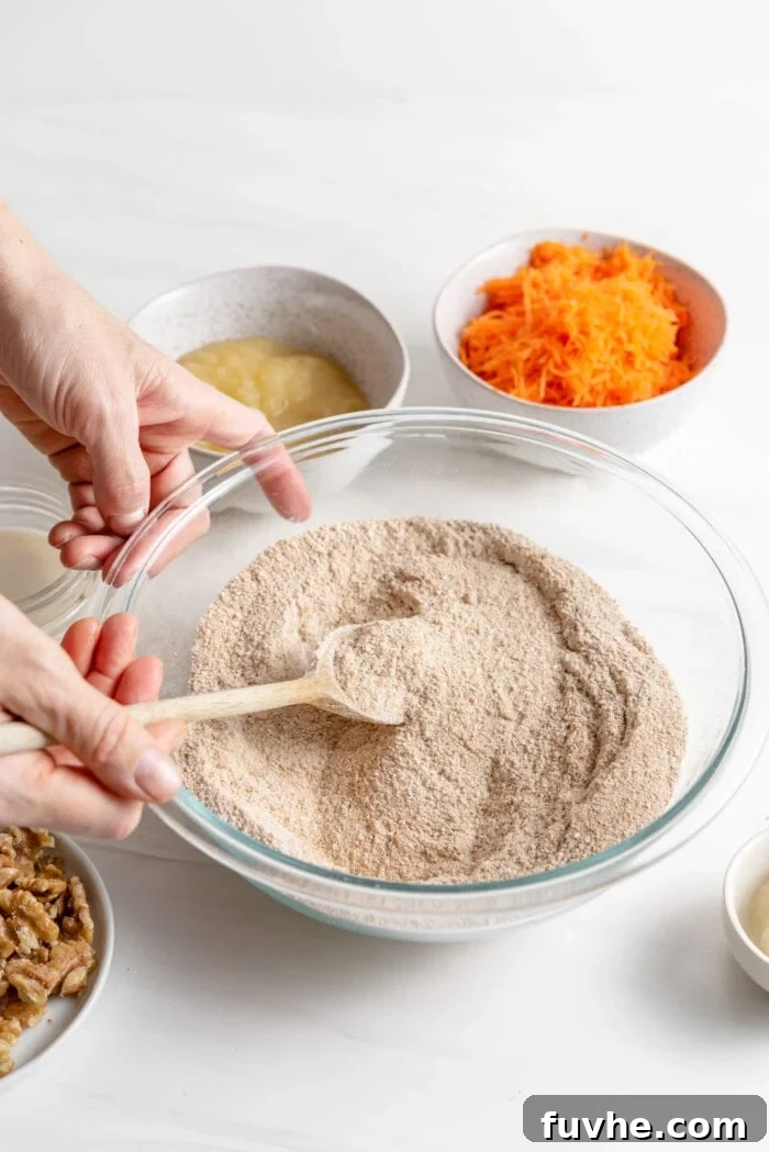 Whisking together whole wheat flour, coconut sugar, baking soda, and a blend of warm spices in a large mixing bowl to create the dry base for the carrot muffins.