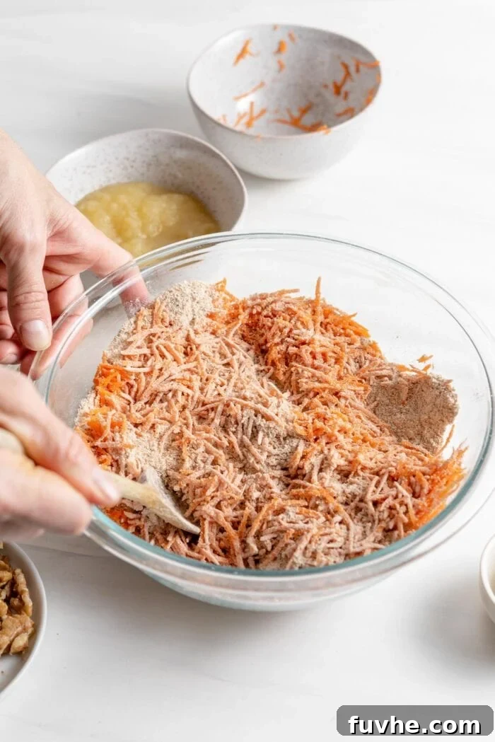 Gently stirring finely shredded carrots into the prepared dry flour mixture in a large bowl, ensuring they are well-coated and evenly distributed before adding wet ingredients.