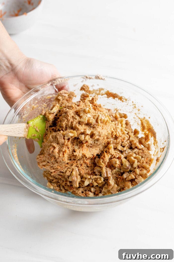 Folding crushed walnuts into the prepared muffin batter using a spatula, ensuring even distribution of the nuts.