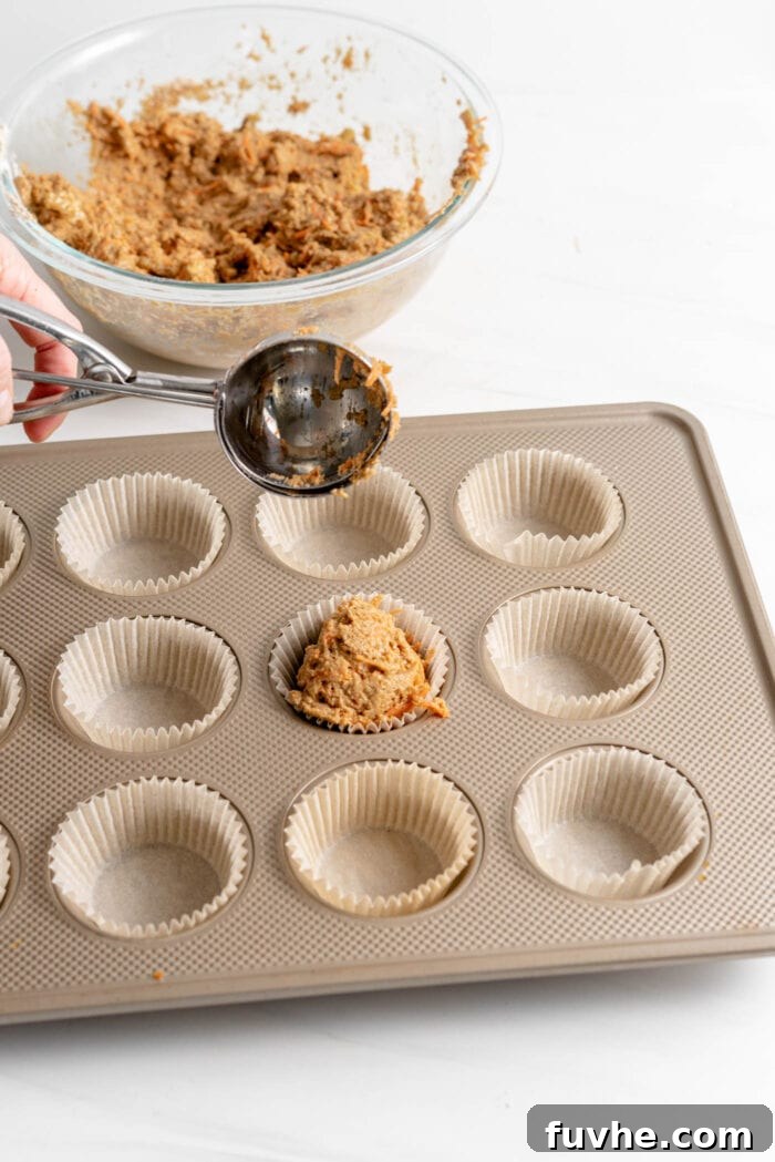 Scooping raw muffin batter evenly into twelve prepared muffin liners in a muffin pan, ready for baking.