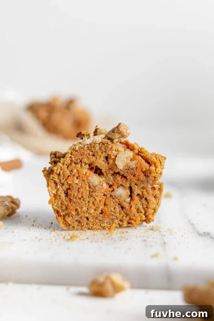 A perfectly baked vegan carrot muffin, sliced open to reveal its moist, tender interior speckled with grated carrots and crunchy walnuts, ready to be enjoyed.