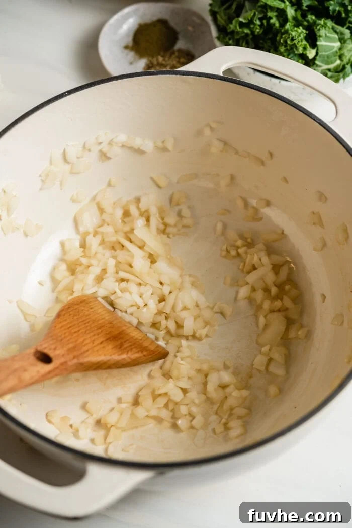 Sautéing chopped onion and garlic in a large soup pot with a wooden spoon, releasing their fragrant aroma.