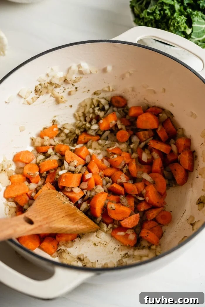 Chopped carrots, onion, and garlic cooking together in a large soup pot, adding color and sweetness.