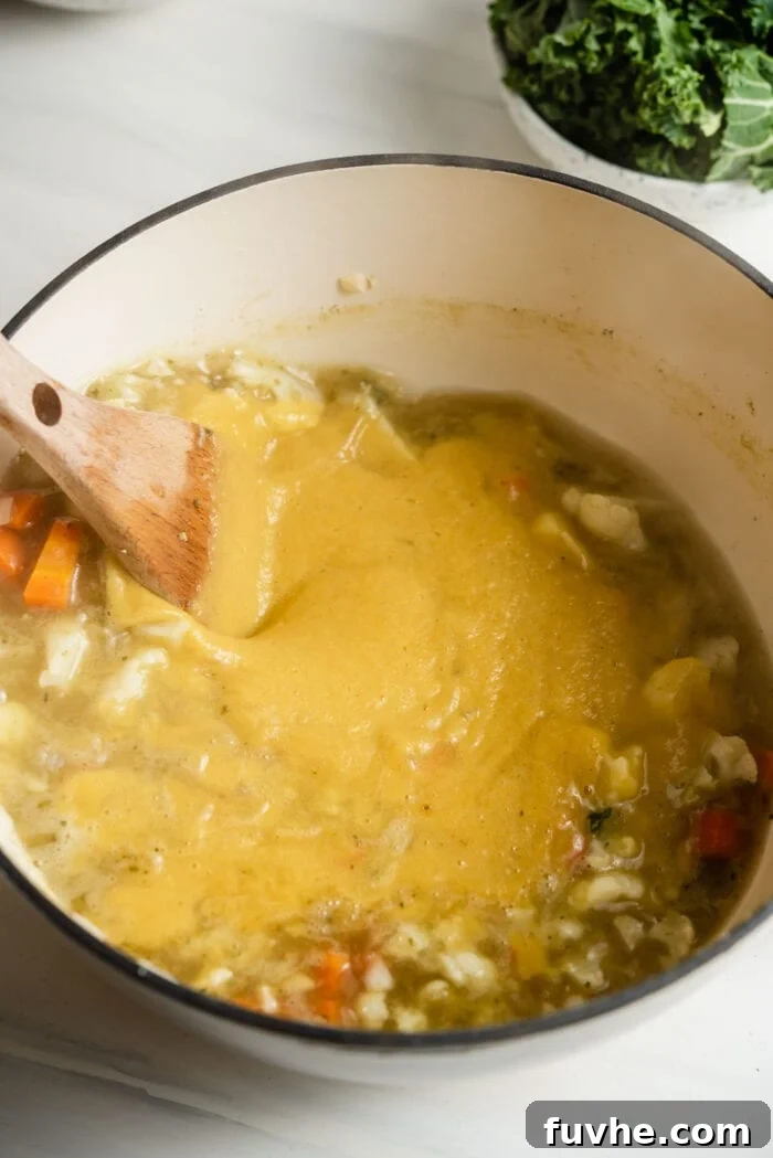 Stirring vegetable soup in a pot with a wooden spoon before blending, showing the rich colors.