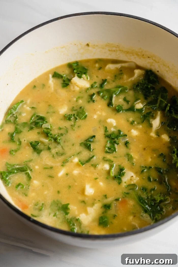 Kale and cauliflower soup in a large pot, with fresh kale stirred in and wilting.