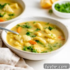 Bowl of kale and cauliflower soup with a spoon in it. Slices of lemon, dish of parsley and another bowl of soup in background.