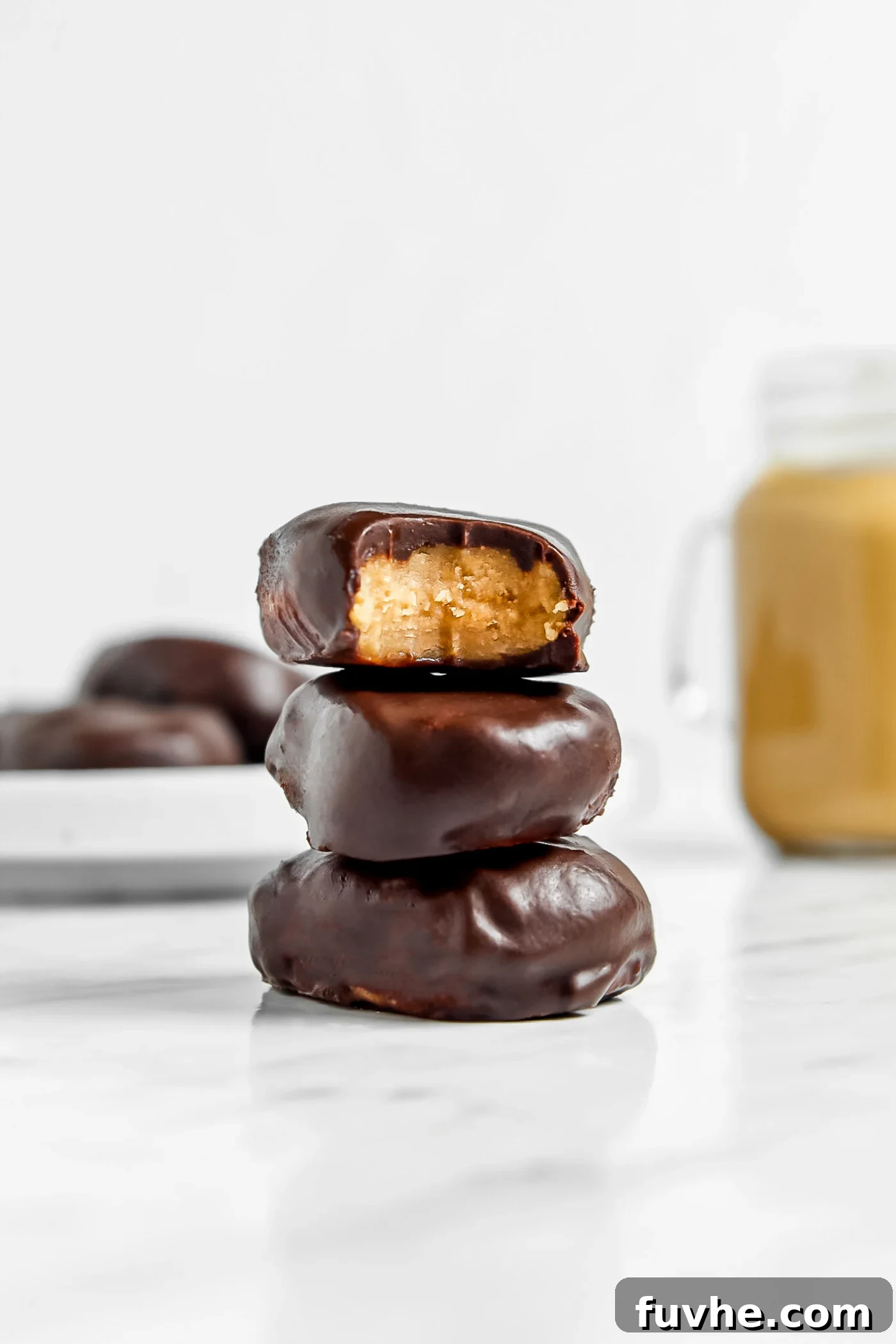 Stack of 3 peanut butter eggs on a marble surface, one on top has a bite out of it showing peanut butter filling.