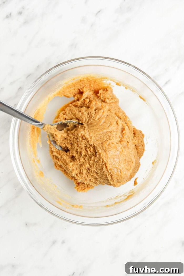 Thick peanut butter batter in a mixing bowl with a spoon.