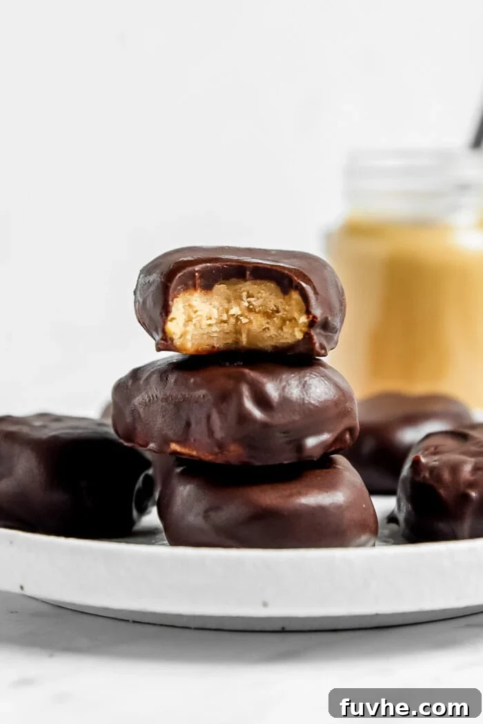 Stack of 3 peanut butter eggs on a plate, one on top with a bite out of it to show the texture inside.