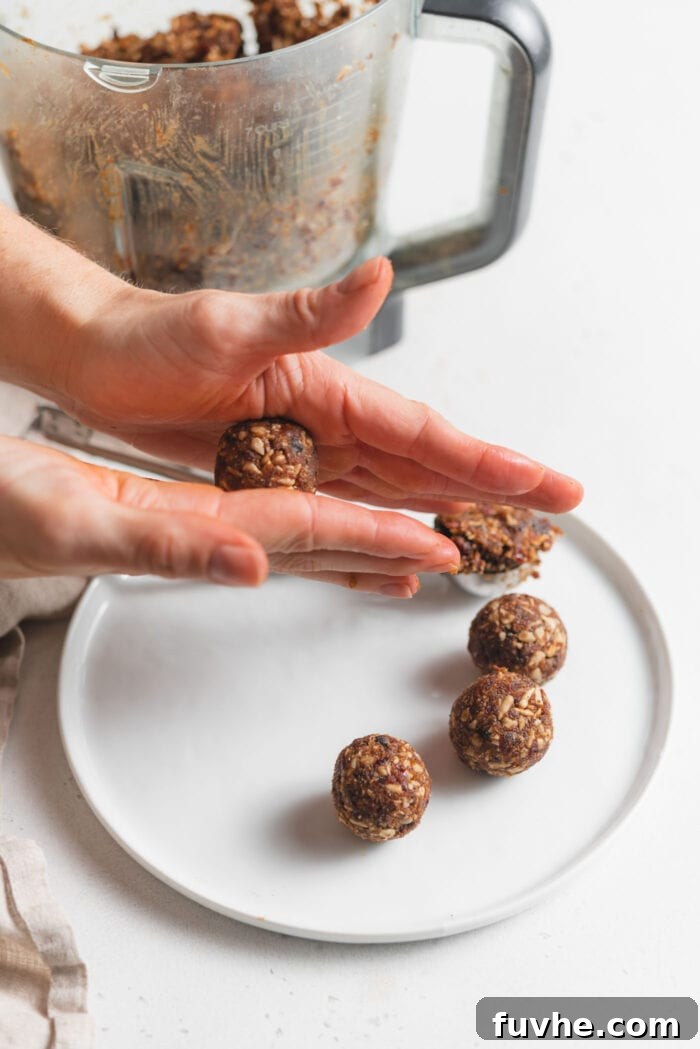 Hands rolling raw energy ball dough into balls over a plate of rolled balls. Shows the process of shaping the uniform energy bites.