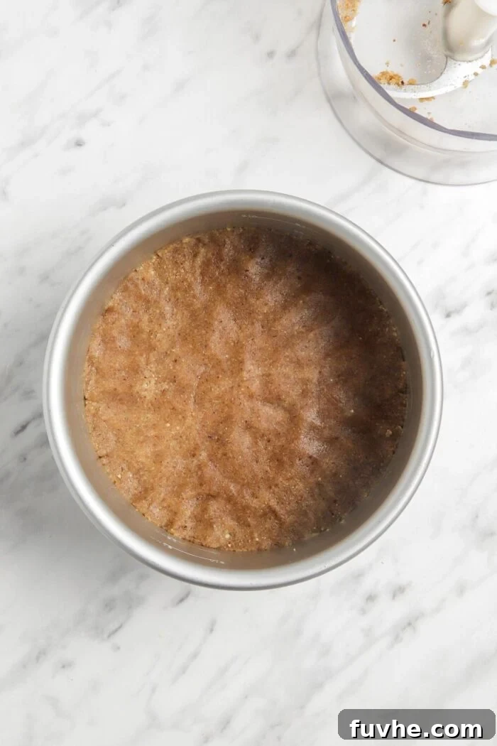 The raw pie crust mixture expertly pressed into an even, flat layer at the bottom of a springform pan, awaiting the filling.