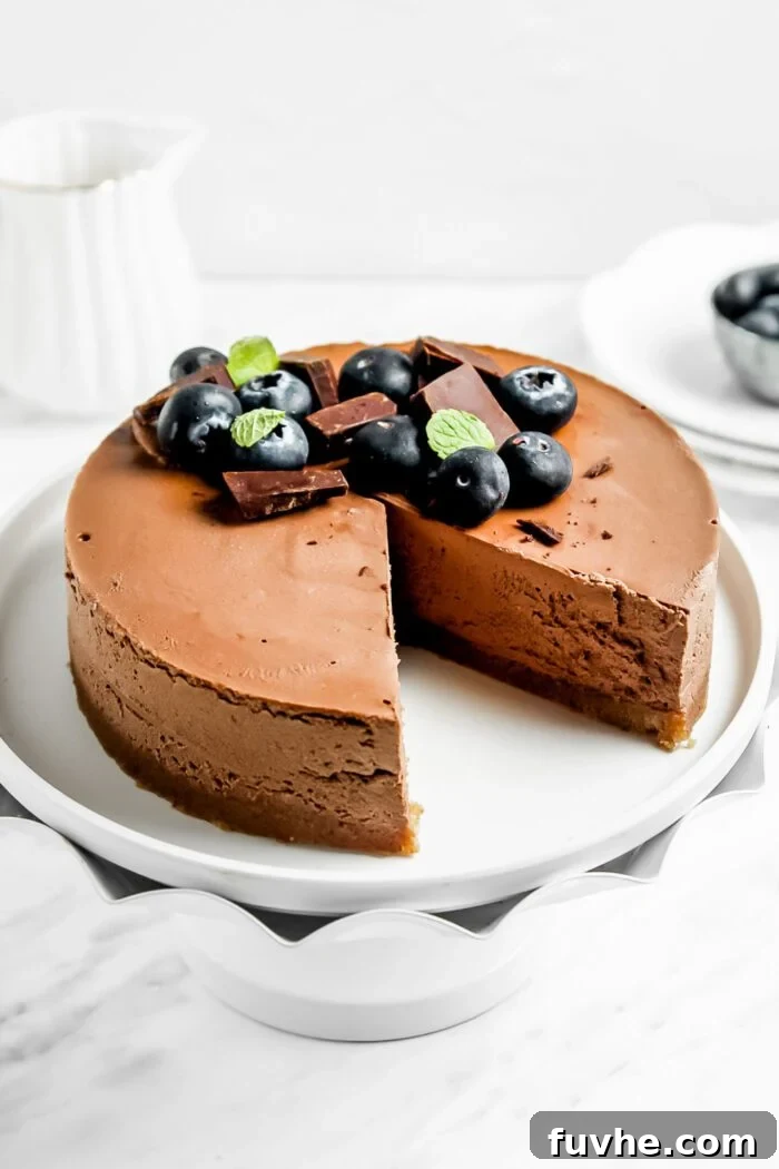 A perfectly sliced raw chocolate cheesecake, with one slice removed and placed on a small decorative plate next to a fork, and the remainder of the cake in the background, all on a cake stand.