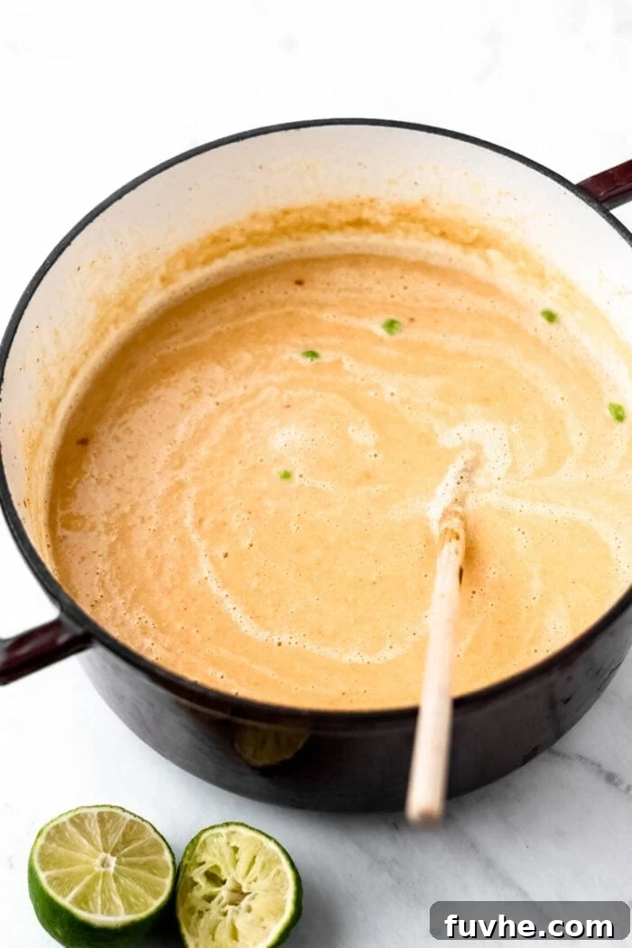A large stock pot full of cauliflower sweet potato soup with green peas in it with a squeezed lime beside it.