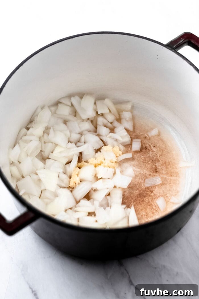 Chopped onions and minced garlic cooking in a large dutch oven with handles.