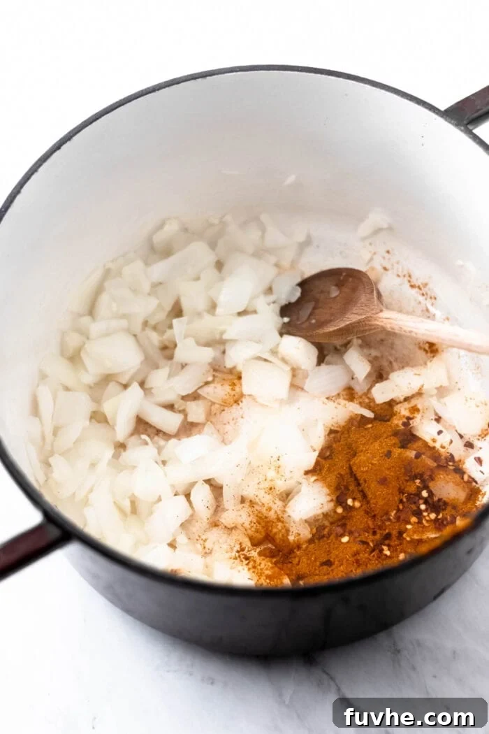 Chopped onion, minced garlic and curry powder cooking in a large soup pot with a wooden spoon.