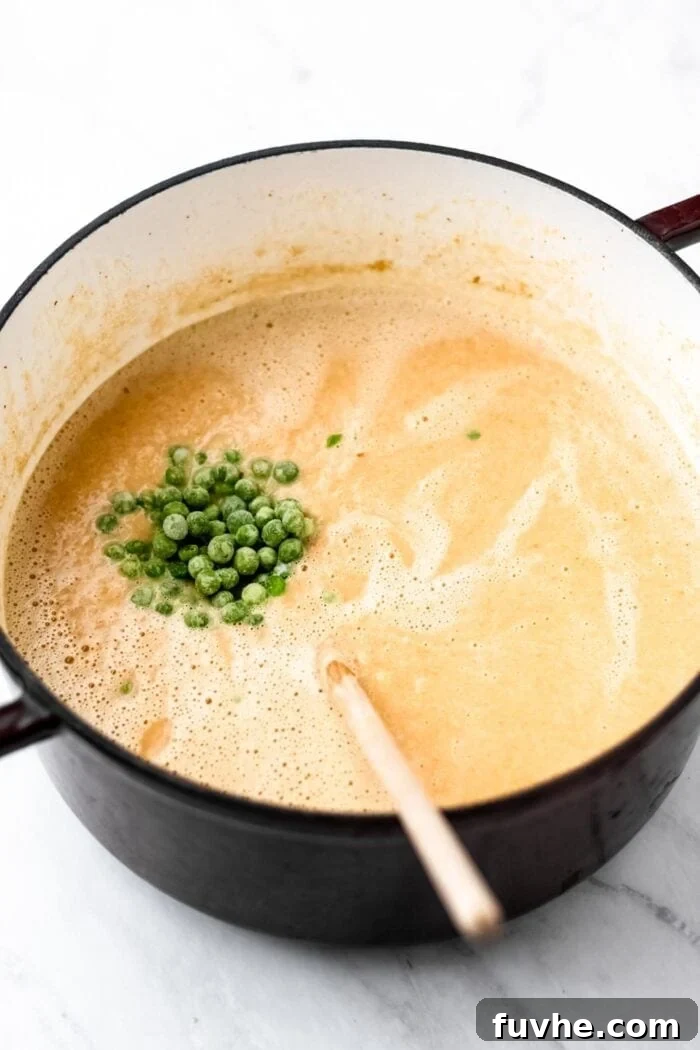 Green peas being stirred into soup in a stock pot.