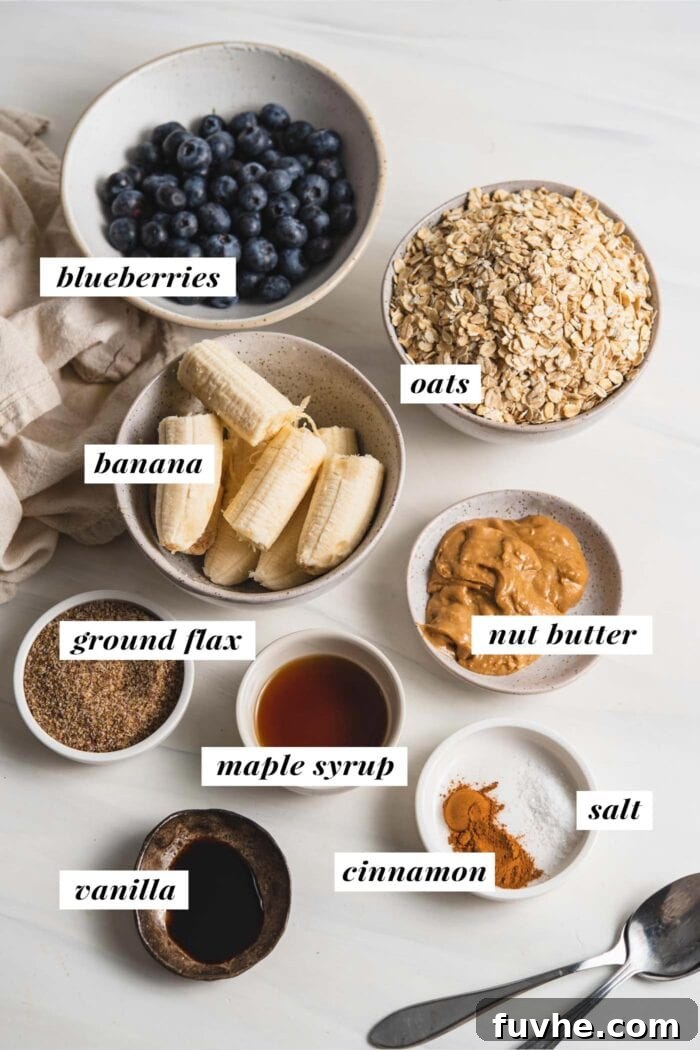 An overhead view of all the wholesome ingredients needed to make baked blueberry oatmeal cups, including ripe bananas, maple syrup, peanut butter, rolled oats, ground flaxseed, cinnamon, salt, and fresh blueberries.