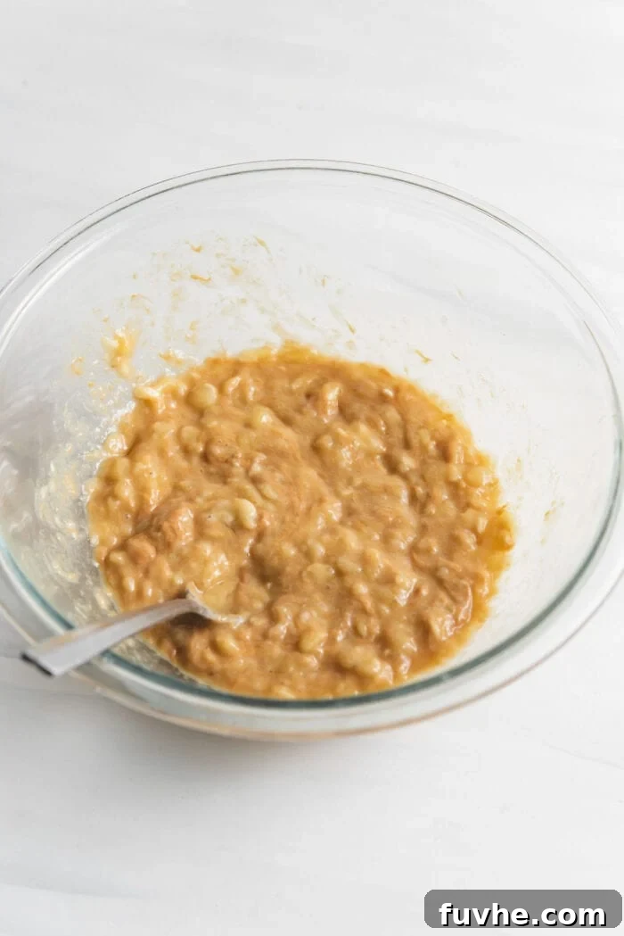 The mashed banana and peanut butter mixture, smooth and combined, in a clear glass mixing bowl.