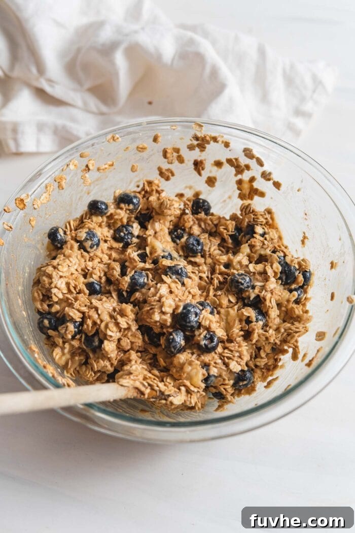 A thick oatmeal batter studded with fresh blueberries, ready for baking, in a glass mixing bowl.