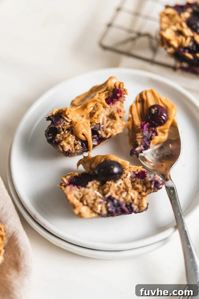 A small, perfectly baked blueberry oatmeal cup, cut in half and generously spread with peanut butter, resting on a plate.