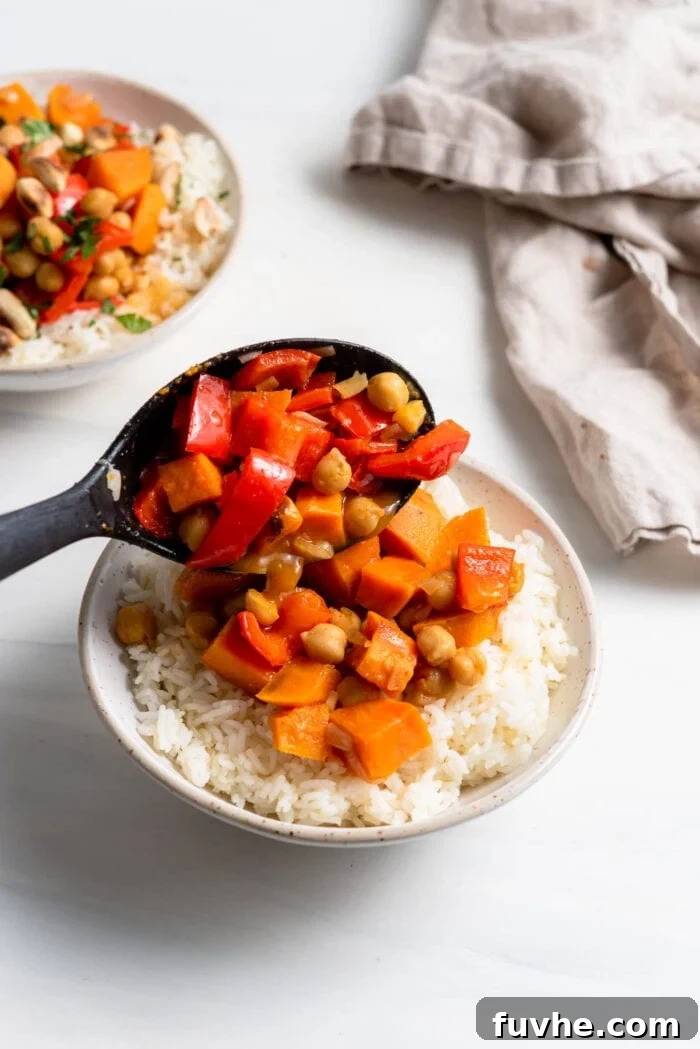 Hearty Sweet Potato Chickpea Coconut Curry 11 A serving spoon gracefully adding a scoop of rich sweet potato curry to a beautifully arranged bowl of garlic rice.