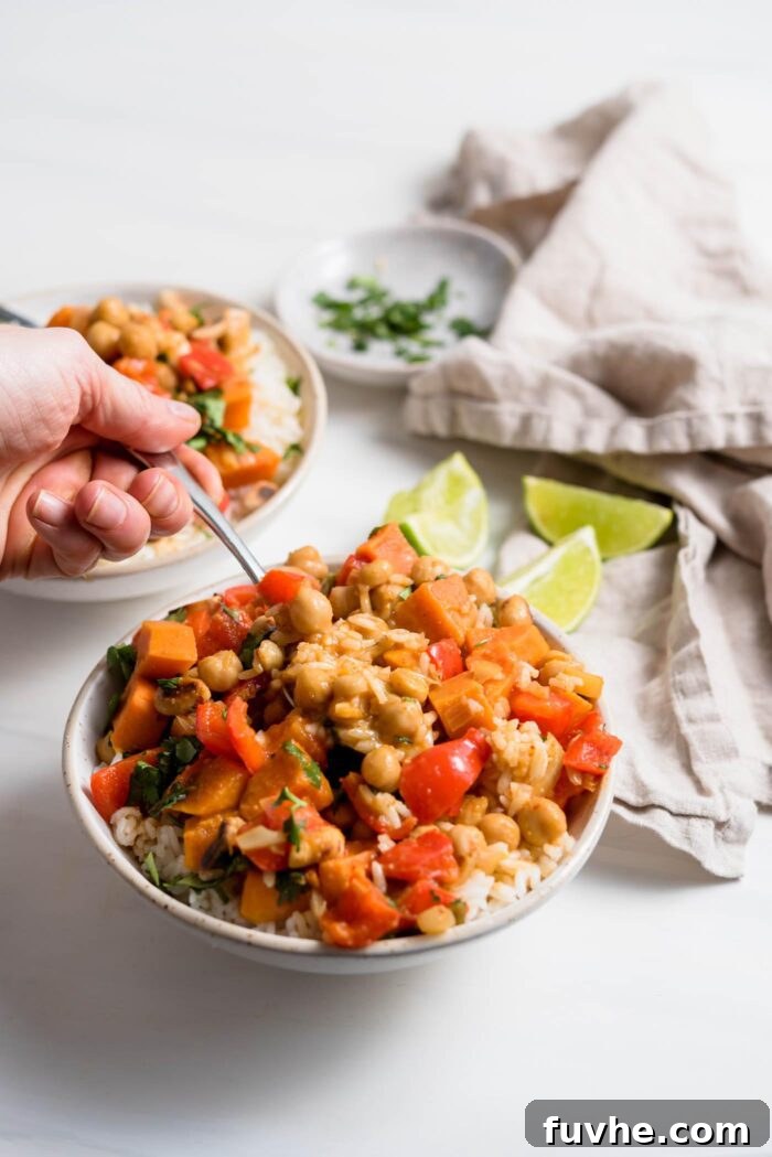 Hearty Sweet Potato Chickpea Coconut Curry 12 A hand holding a spoon, scooping a generous portion of creamy sweet potato chickpea curry from a rustic bowl, ready to be enjoyed.