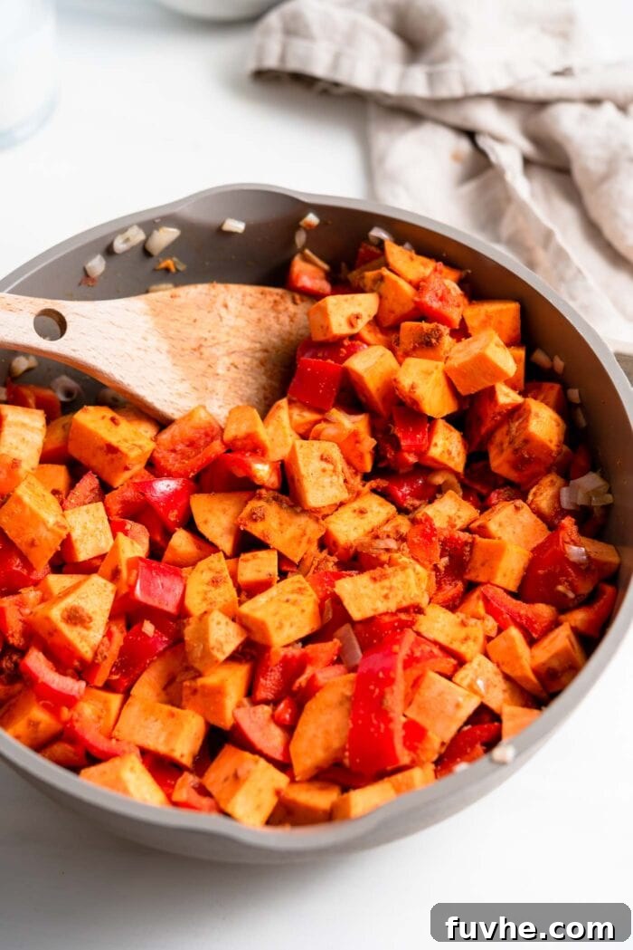 Hearty Sweet Potato Chickpea Coconut Curry 7 Colorful sweet potato cubes and chopped bell pepper being sautéed with aromatic spices and curry paste in a wide skillet.