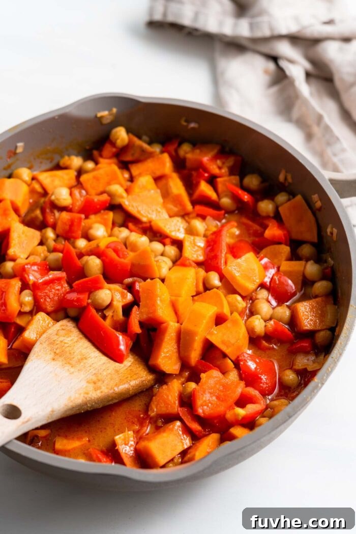 Hearty Sweet Potato Chickpea Coconut Curry 9 A vibrant sweet potato and chickpea curry gently simmering in a large skillet, its rich sauce visibly thickening.