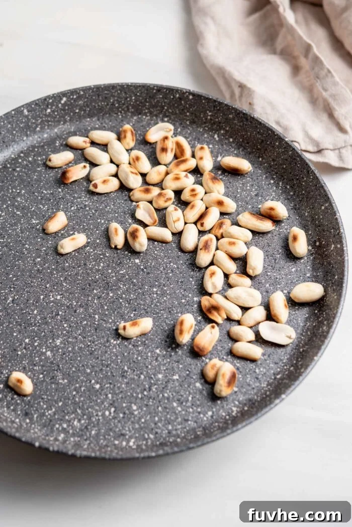 Hearty Sweet Potato Chickpea Coconut Curry 10 Chopped peanuts being toasted in a dry skillet on the stovetop, turning golden brown for a crunchy topping.
