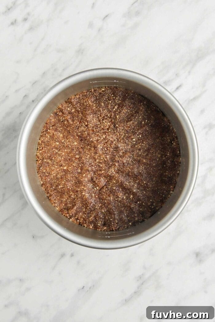 A perfectly prepared, golden-brown pie crust made from pecans, pressed firmly into the base of a springform pan, awaiting the creamy filling.