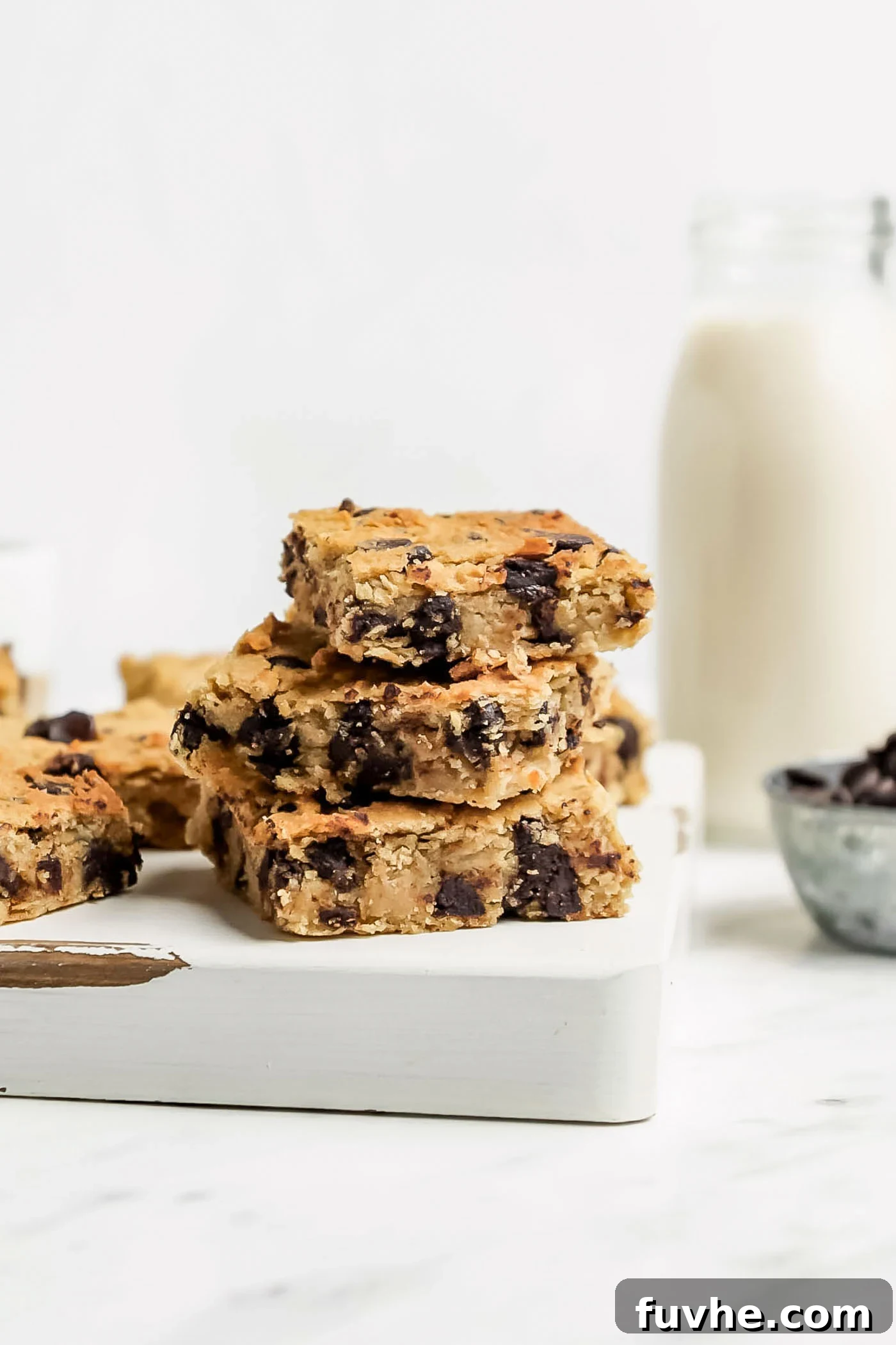 Stack of 3 chocolate chip blondies on a cutting board, highlighting their golden brown exterior and chocolatey interior.