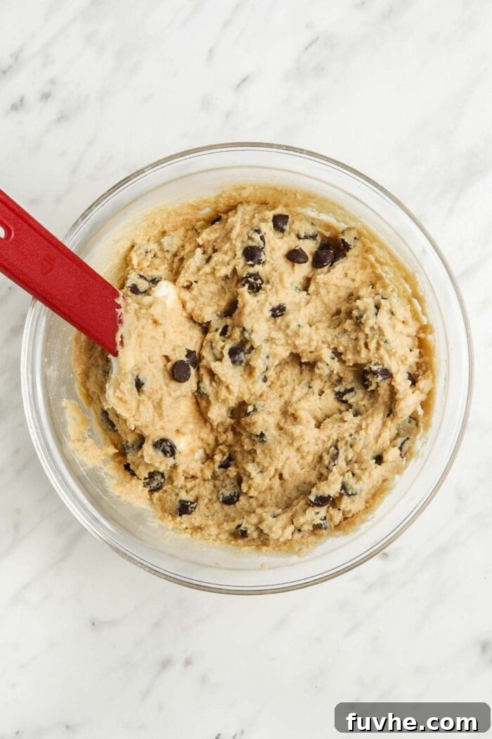 Chocolate chip blondie batter in a bowl with a spatula, after chocolate chips have been folded in.