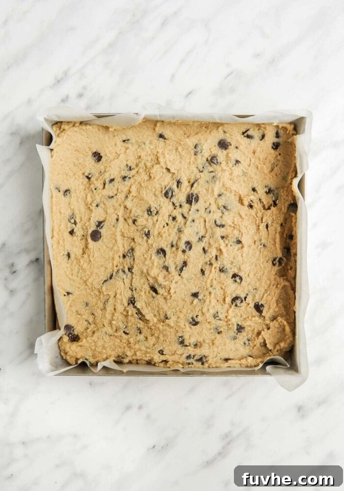 Raw chocolate chip blondie batter in a baking pan, smoothed out and ready for the oven.