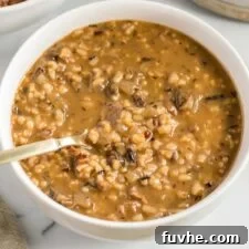 An overhead shot of a single bowl of rich, creamy vegan mushroom wild rice soup, garnished with fresh herbs and a spoon, inviting you to savor its comforting flavors.