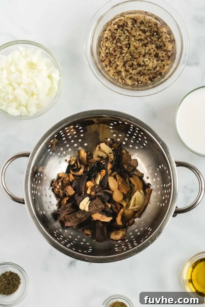 Rehydrated mixed dried mushrooms, along with garlic and a bay leaf, being strained over a bowl to preserve the deeply flavorful soaking liquid.