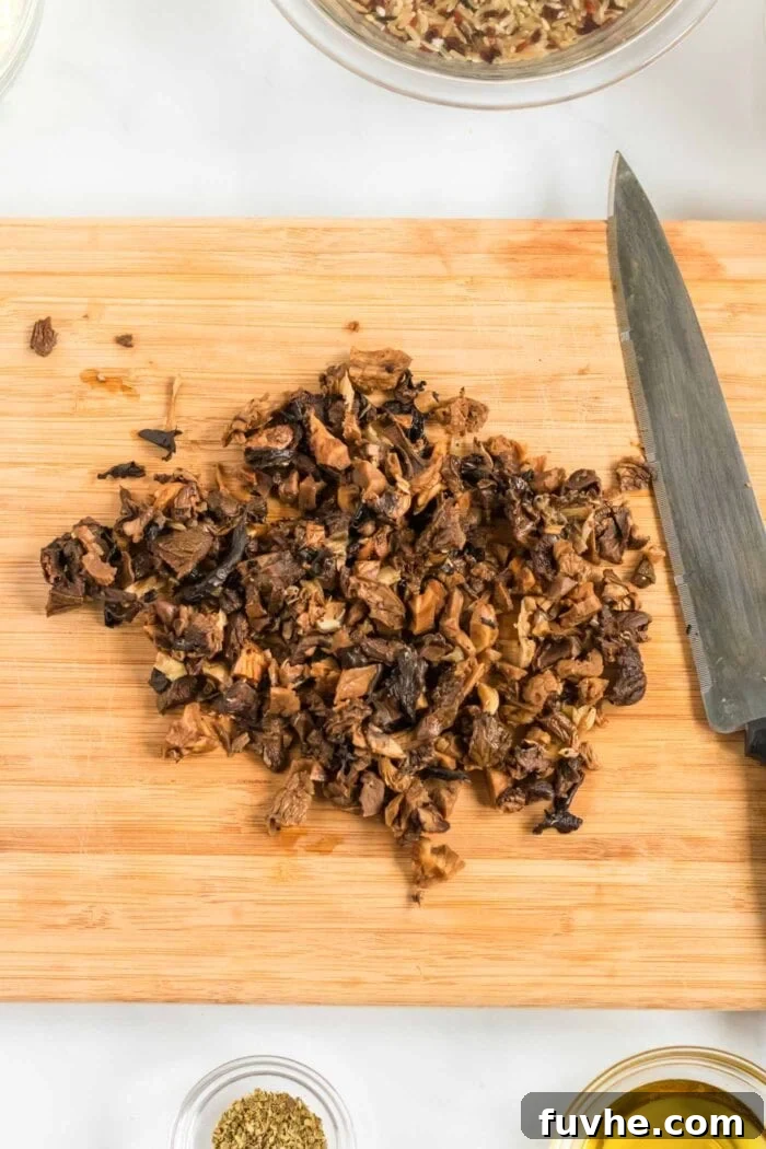 A neat pile of finely chopped rehydrated mushrooms on a wooden cutting board, prepped and ready for incorporation into the soup.