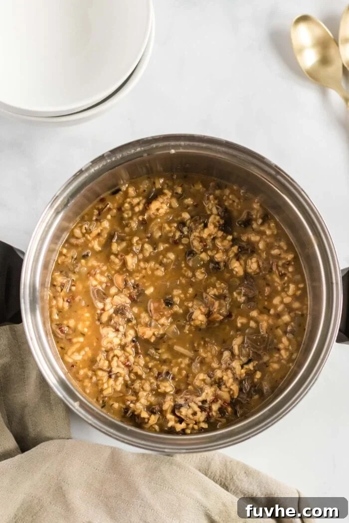 A rich, thick, and steaming pot of mushroom wild rice soup, filled with grains and vegetables, simmering on the stovetop.