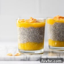 A glass jar of layered mango chia pudding topped with coconut flakes. Another jar of pudding is in the background.