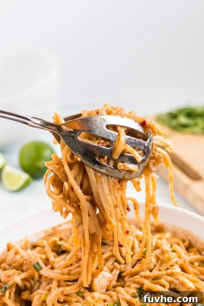 A pair of tongs lifting a generous portion of perfectly coated Pad Thai noodles from a large serving bowl, highlighting the texture and rich color of the dish, ready to be plated.