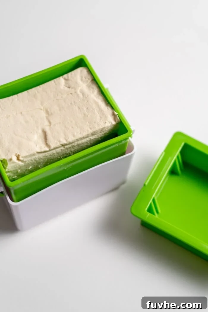 A block of extra-firm tofu being pressed in a specialized tofu press, demonstrating the initial preparation step for making crispy tofu.