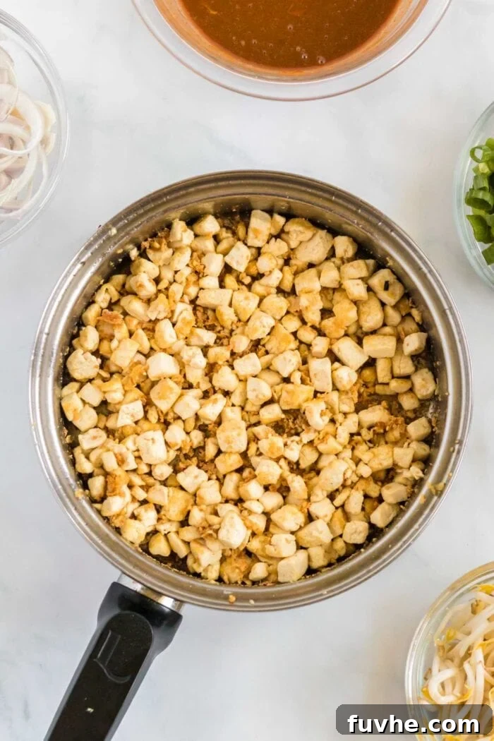Diced pieces of extra-firm tofu, pan-fried to a golden brown and crispy perfection, shown in a large saucepan. The tofu exhibits a beautiful crust, indicating ideal cooking.