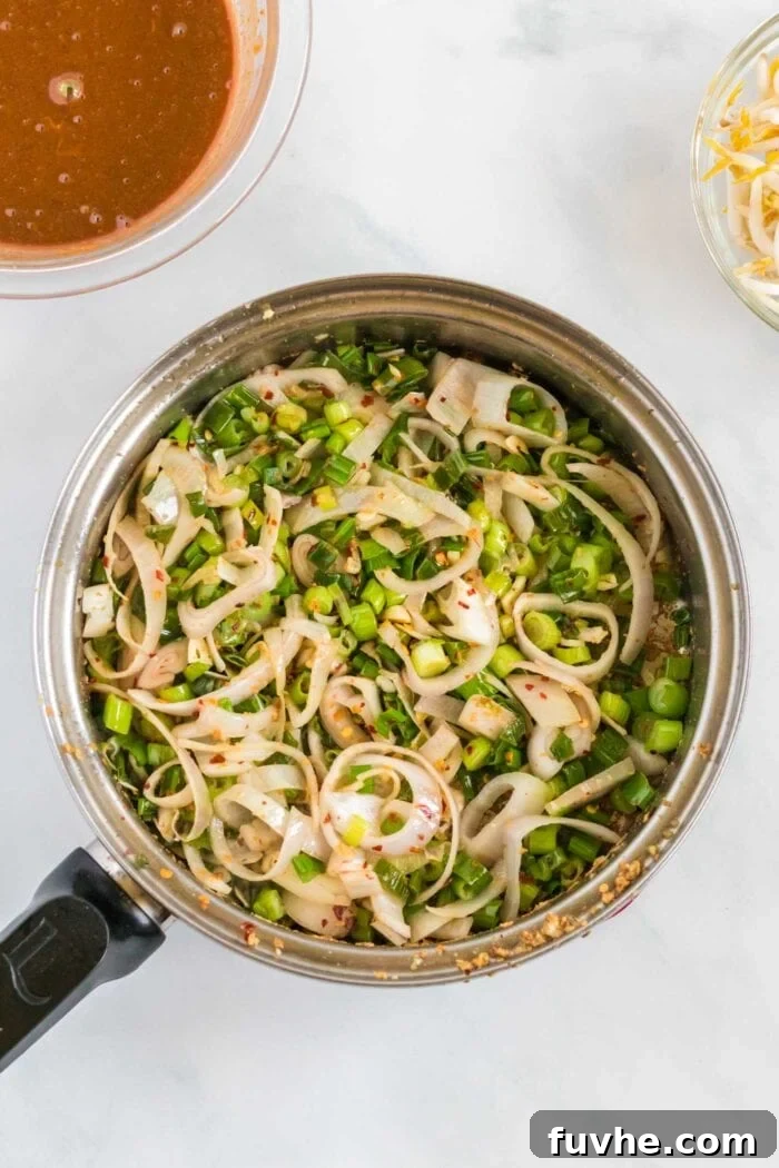 Finely minced garlic, thinly sliced shallots, and chopped green onions sizzling in a skillet with a small amount of sesame oil, releasing their fragrant aromas as they cook.